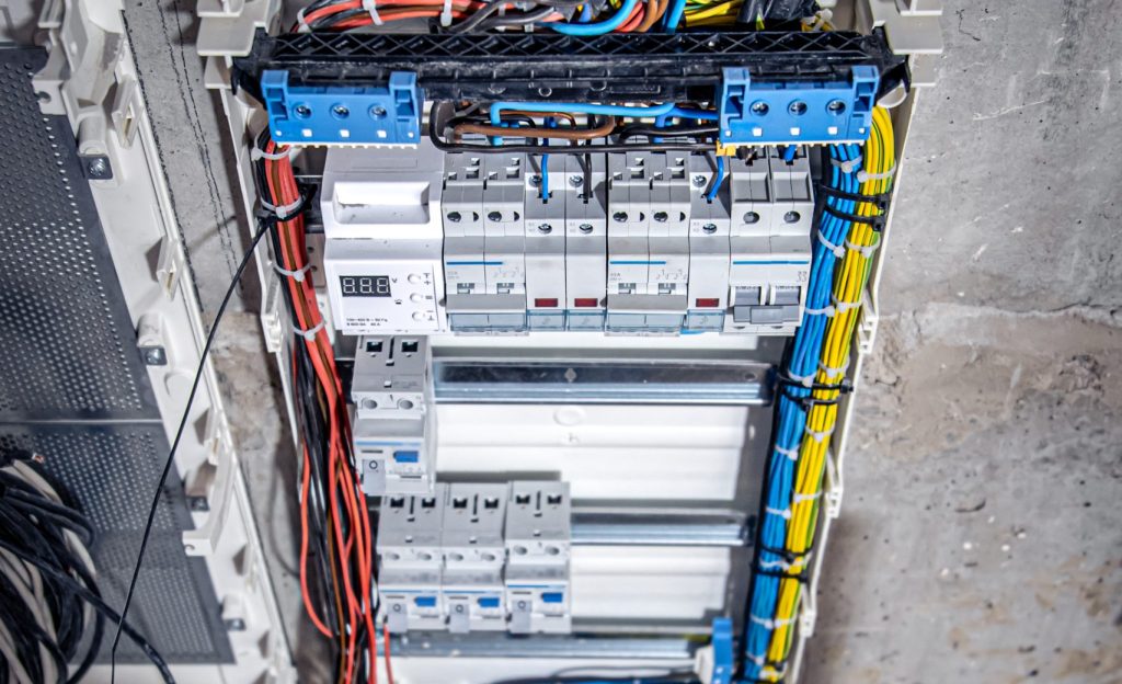 a male electrician works in a switchboard with an electrical connecting cable.